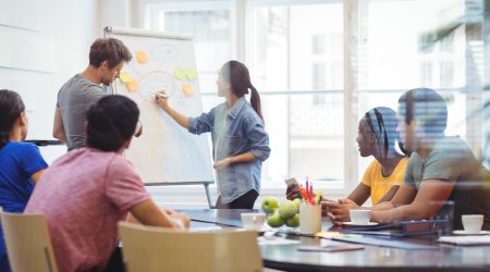 Business executives discussing with their colleagues on whiteboard during meeting at office